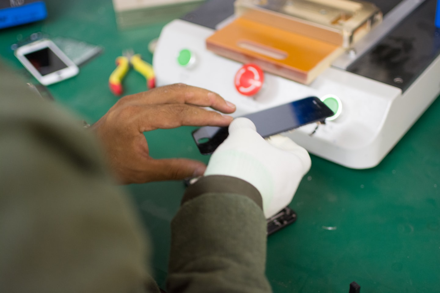Technician repairing a smartphone on a green workbench.