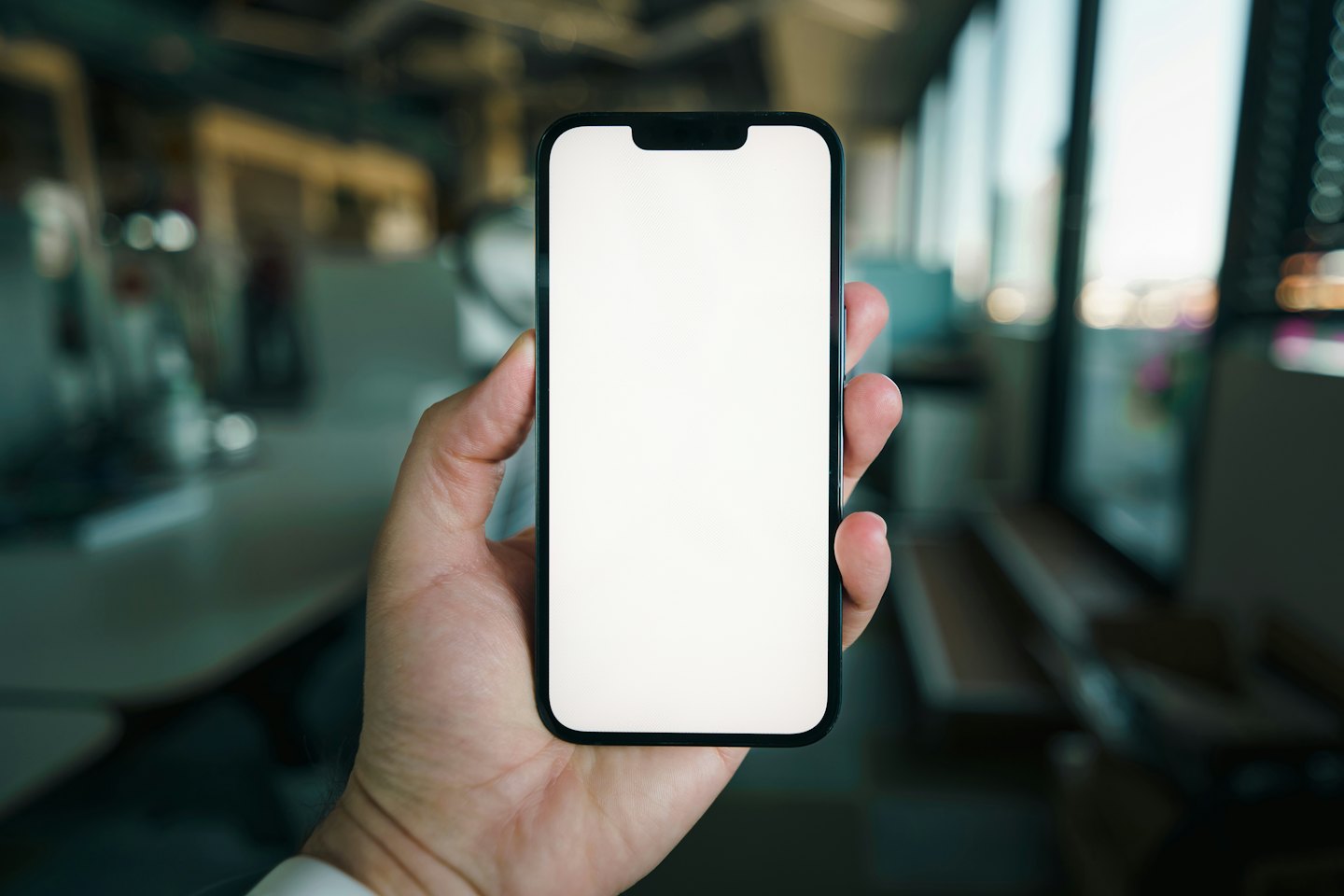 Hand holds modern smartphone with blank white screen.